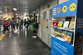 Fotografia de uma estante com livros, dentro da estação do metrô.